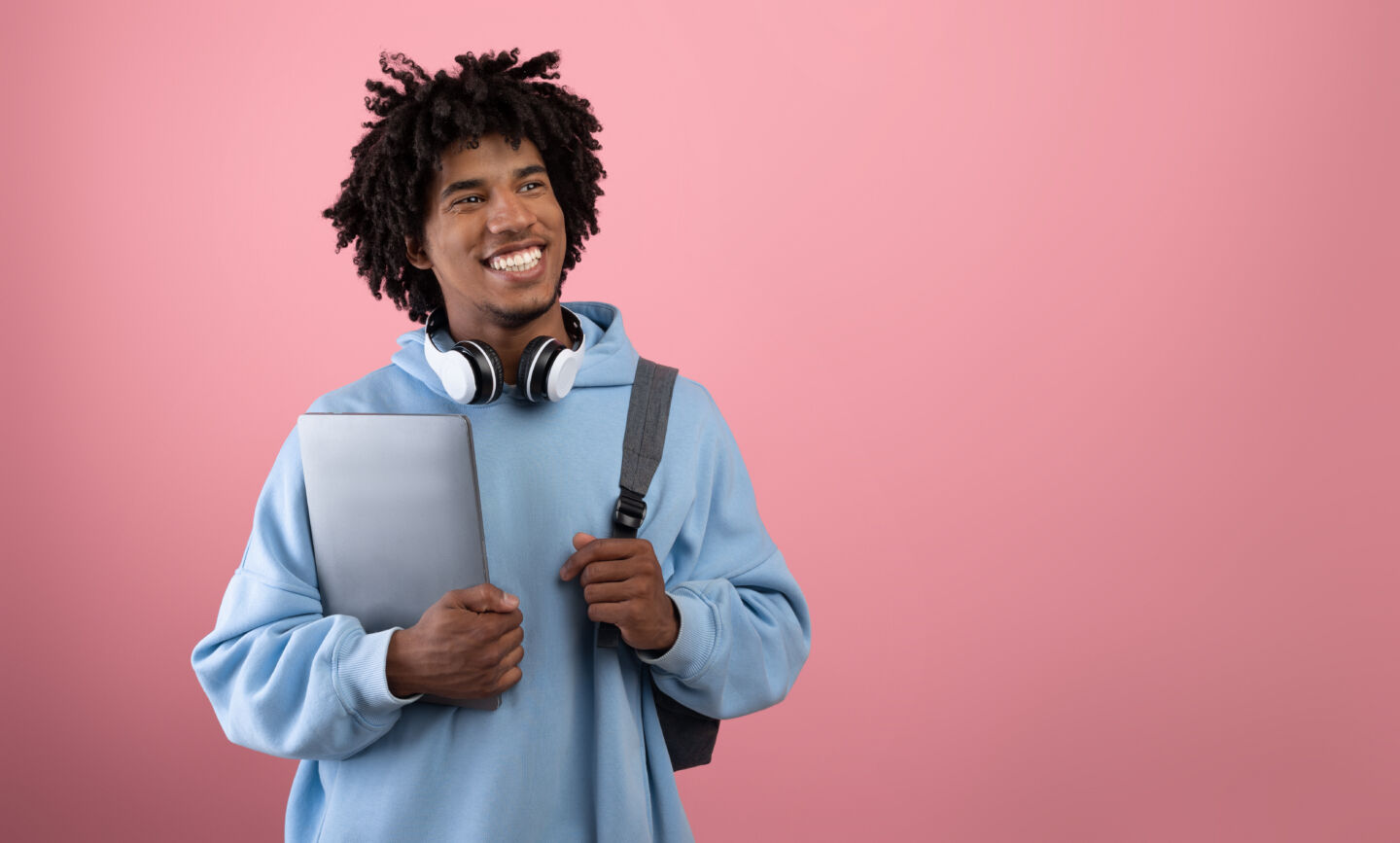 Positive African American teen student with backpack, tablet pc and headphones studying online on pink studio background, banner with free space. Happy black adolescent having remote college education